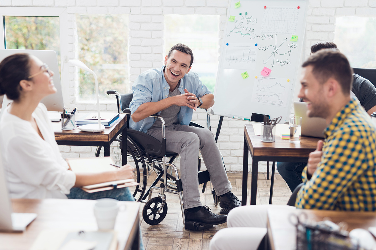 Several employees, including one in a wheelchair, collaborate in an ability diverse workplace.