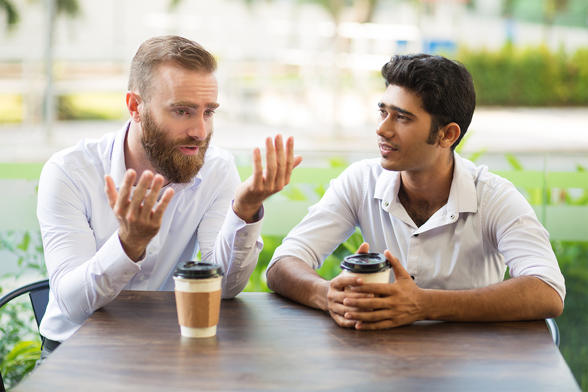Two men discuss mental health at a table outside while drinking coffee on Bell Let's Talk Day.